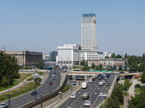 Krakow, Lesser Poland Voivode, Poland - 04 August 2026: Aerial view of Unity Tower and surrounding office buildings with busy traffic on the roads, green trees, and a clear blue sky.