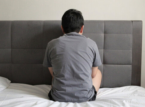 A person sits comfortably on the edge of a bed in a cozy bedroom setting, great for use as a placeholder or to illustrate a scene
