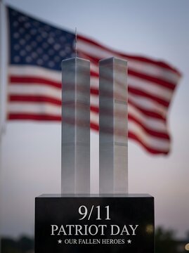 Patriot day 9 11 remembrance with twin towers model and american flag waving in background honoring fallen heroes on dark monument.