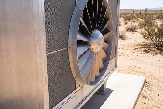 A direct air carbon capture unit with a large metal fan stands in a sunny desert landscape.