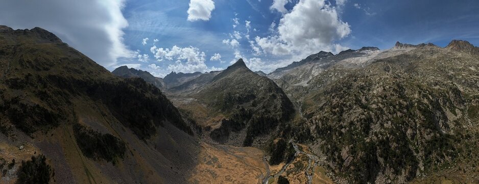 Wide panoramic view of the spectacular Benasque Valley in the Spanish Pyrenees, Aragon, Spain. Rugged rocky peaks, deep mountain valleys and dramatic summer clouds create a wild high-altitude landscap