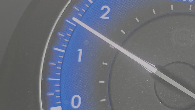Detailed close up of a modern car's dashboard with the tachometer needle moving, indicating engine revolutions and idle speed