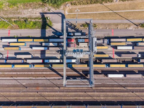 Karlsruhe, Baden-Wurttemberg, Germany - 29 July 2026: Aerial view of an intermodal freight terminal with a gantry crane loading shipping containers onto railway wagons.