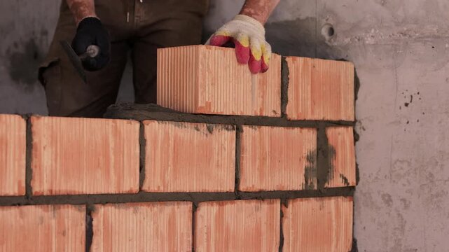 Worker placing ceramic brick on mortar during wall construction close up
