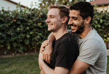 Fototapeta premium Happy gay couple embracing outdoors, smiling and looking away, love, relationship, and togetherness