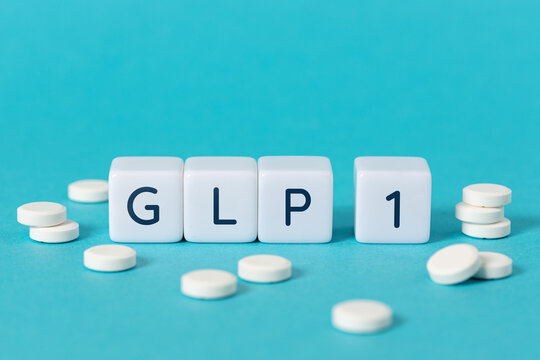 GLP 1 word on blocks surrounded by medicine pills on blue background. Copy space