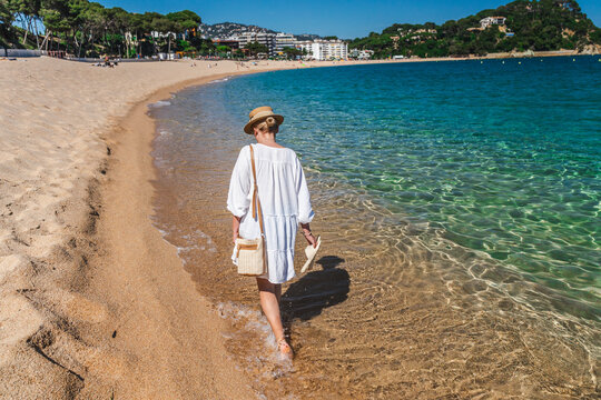 Woman walking along shoreline of Lloret de Mar beach with crystal clear water