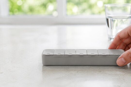 Mujer toca un objeto gris sobre una mesa con un vaso de agua al fondo