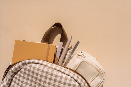 School backpack filled with notebooks, pens and pencil case in warm sunlight.