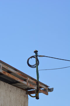 An electrical service mast with a weatherhead and drip loop is attached to the edge of a building roof under a clear blue sky