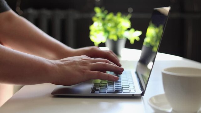 Close-up of hands typing on a laptop with a coffee cup nearby