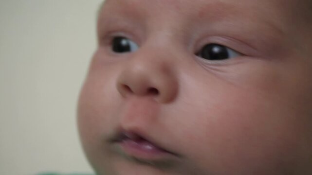 Close-up infant face with slight lip movement, moist lower lip, focused gaze, gentle head turn and calm curious expression, showing soft skin detail, intimate view and subtle motion
