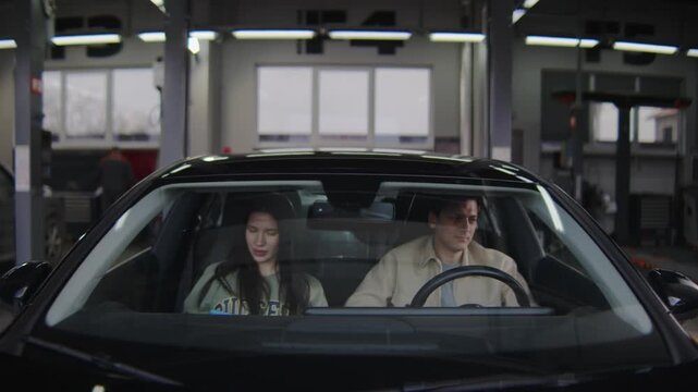 A premium-class car pulls out of a repair and maintenance bay, with attractive young people sitting inside. 