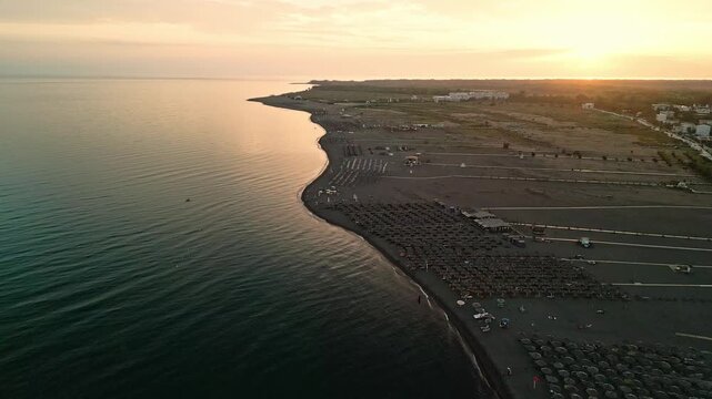 Albania, Velipoja 12 09 2025: Drone video moving backward along Velipoja beach with sea water reflecting sunset light, rows of sun umbrellas and wooden path on sand.