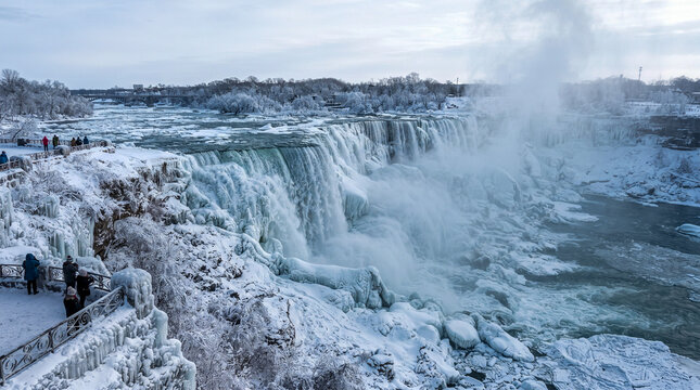 Impresionante vista invernal de las cataratas del Ni&aacute;gara rodeadas de nieve, hielo y rocas congeladas bajo un cielo fr&iacute;o y nublado.
