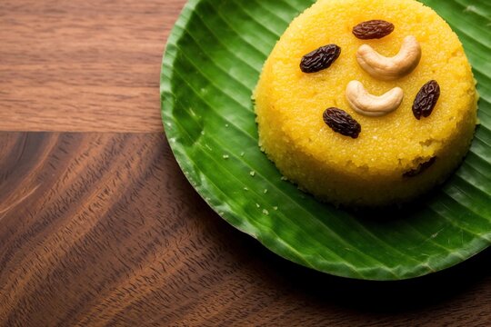 Yellow sweet semolina cake served on green banana leaf. Traditional Indian dessert suji halwa with raisins, cashew nuts on wooden table. Tasty South Asian breakfast food festive snack for
