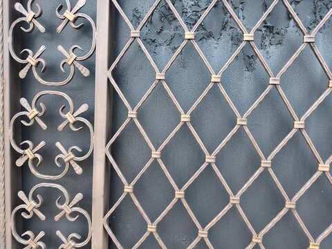 A weathered metal gate with intricate scrollwork and diamond mesh stands against a textured gray wall, evoking themes of confinement and decay. Abandonment and forgotten boundaries