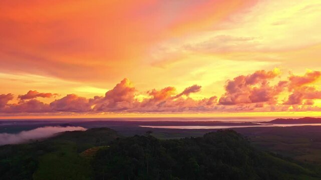  Aerial view of  A serene valley lies beneath a golden sky as soft fog flows like a river. The rising sun casts radiant beams that turn every cloud into a brushstroke of living color.