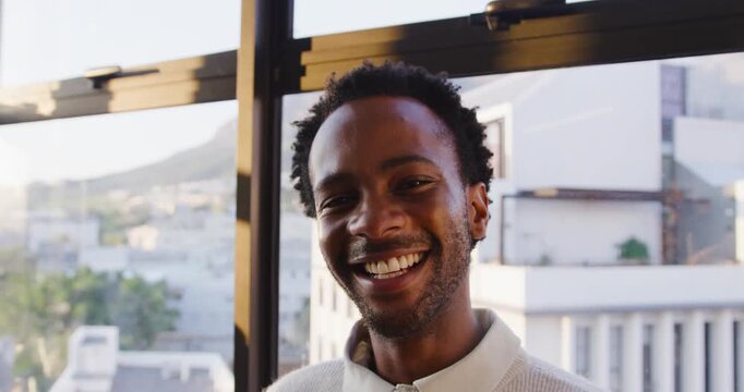Engaging with camera African American man in late 20s in light top smiling, laughing, facing window