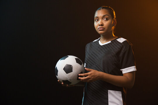 African American woman holding soccer ball at waist in studio in black-and-white jersey, copy space