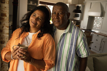 Mature African American couple standing in warm home kitchen holding ceramic mug and jewelry © wavebreak3