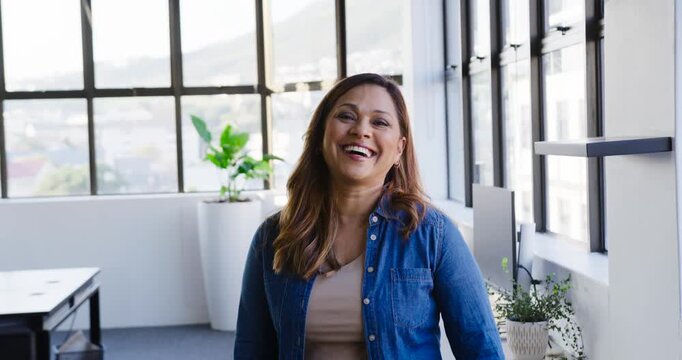 Mature African American woman responding to off-camera joke, smiling and laughing by grid windows