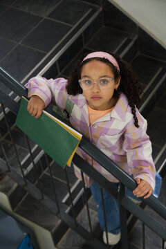 African American child standing on tiled stairwell grasping metal handrail holding green folder