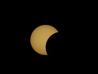 A partial solar eclipse appears as a golden crescent against a black sky over Mioglia, Italy, revealing visible sunspots on the solar surface. © Roberto