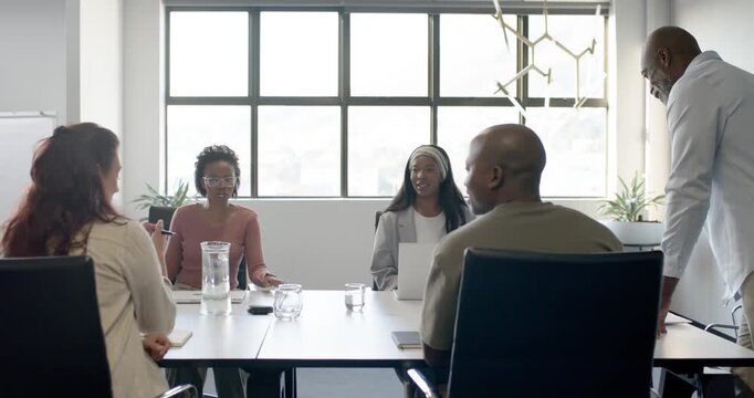 African American woman in pink presenting update at table after manager cue, gesturing near laptop