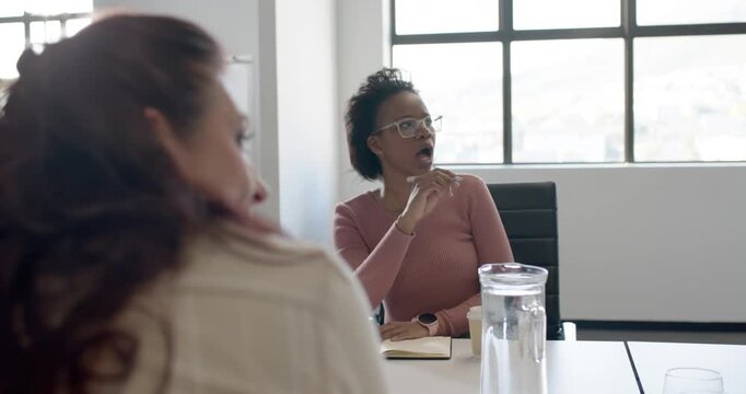 Shot panning to adult African American woman raising pen over notebook, leading meeting at table