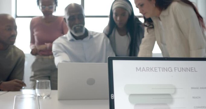 Diverse coworkers leaning around laptop and monitor, responding to marketing funnel, aligning plan