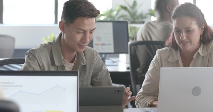Diverse coworkers reviewing tablet and laptop, man tapping while woman leaning in comparing charts