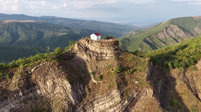 Clockwise drone orbit around a solitary Orthodox chapel on a sunlit cliff, evoking the legendary Georgian story of a blessed land gifted by God amid the grandeur of the Caucasus