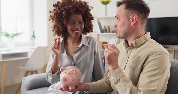 Couple planning savings with piggybank at home. They add coins, discuss budget and finance, and set goals for investment and an emergency fund. Clear concept of budgeting and money saving.