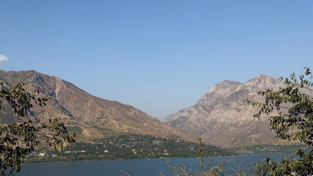 Scenic view of Charvak Reservoir in the mountains near Tashkent, Uzbekistan, surrounded by rugged mountains and lush greenery.