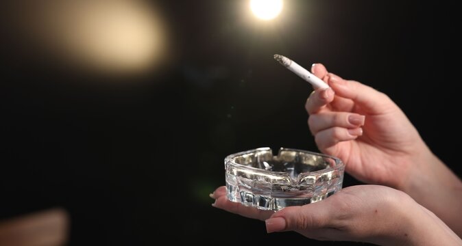 Woman flicking ash from cigarette into ashtray on black background, closeup. Space for text