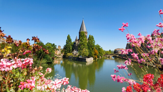 Temple Neuf standing on island in Moselle river, surrounded by trees and colorful flowers