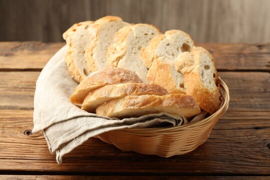 Fresh bread slices in wicker basket on wooden table, closeup