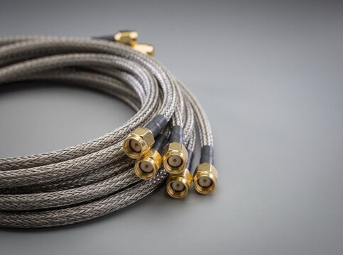 Coiled braided coaxial microwave cables with gold SMA connectors on a gray background
