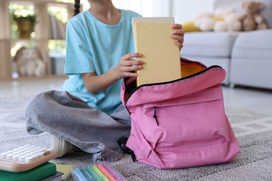 Girl packing her backpack for school on floor at home, closeup