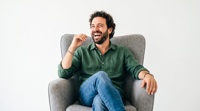 Happy man laughing while sitting in a grey armchair against a white background