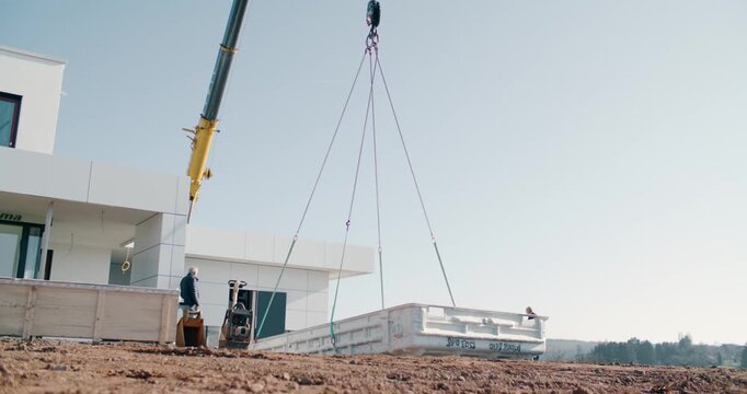 Construction crane lifting heavy load on a modern building site, construction worker operating machinery outdoors at a residential real estate development project, wide shot under clear sky