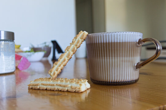 A glass cup of layered latte coffee with two crisp butter cookies resting on a wooden table.