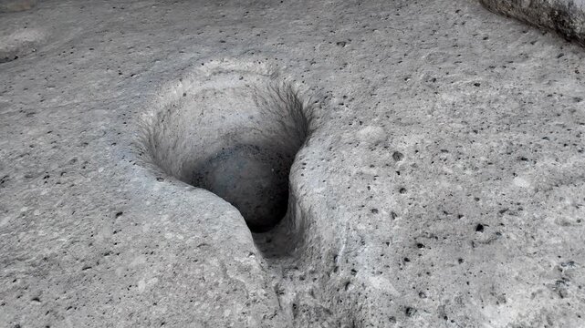 Slow camera movement shows an ancient mortar and pestle embedded in the stone floor of the cave, revealing details of a primitive tool for grinding Vardzia grains, seeds, or minerals