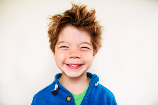 Portrait of a smiling boy with messy hair standing in front of a white wall