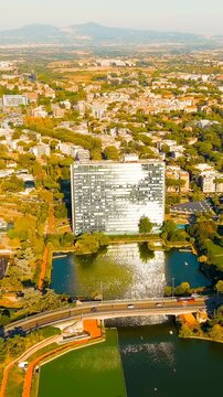 Vertical video. Rome, Italy. The artificial lake of EUR district, a vast modernist urban complex with a glass-fronted building reflecting on the water, Drone footage under clear summer sky. Drone foo