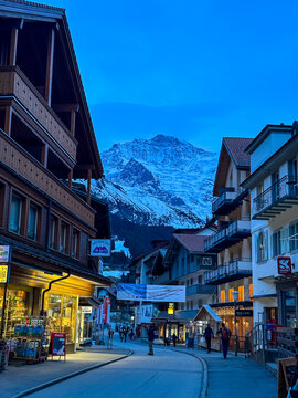 Wengen, Switzerland - March 13, 2026. An atmospheric evening view looking down the main pedestrian street of Wengen, Switzerland. Warm, golden light spills from shopfronts like Skiset Wengen and tradi