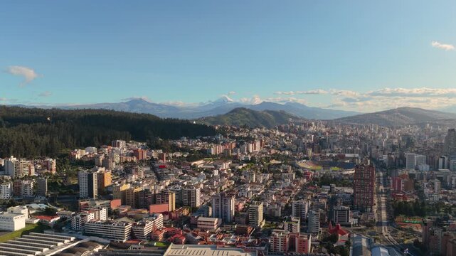 Drone view of Quito, Ecuador showing the financial district, Atahualpa Olympic Stadium, and Cotopaxi volcano in the distance beneath a clear Andean sky.