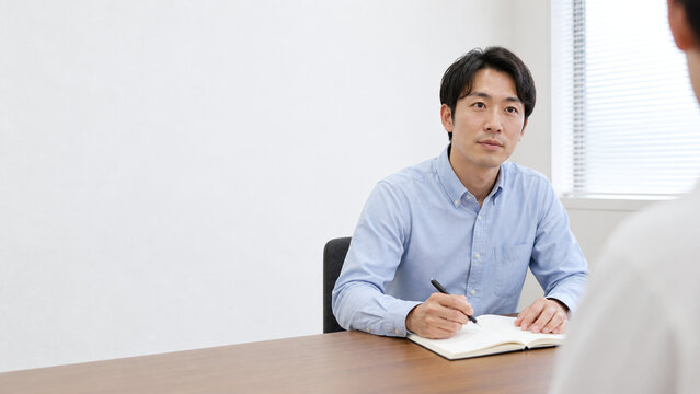 ノートを取りながら話を聞く日本人男性 面談と余白のある背景