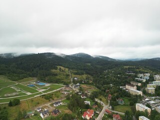 Krynica-Zdrój - Polska Panorama miasta i okolicznych gór nagrana dronem. Jaworzyna Krynicka, Góra Parkowa, miasto, Beskidy, lasy, mgła i chmury nisko osadzone opadające na góry © Konrad